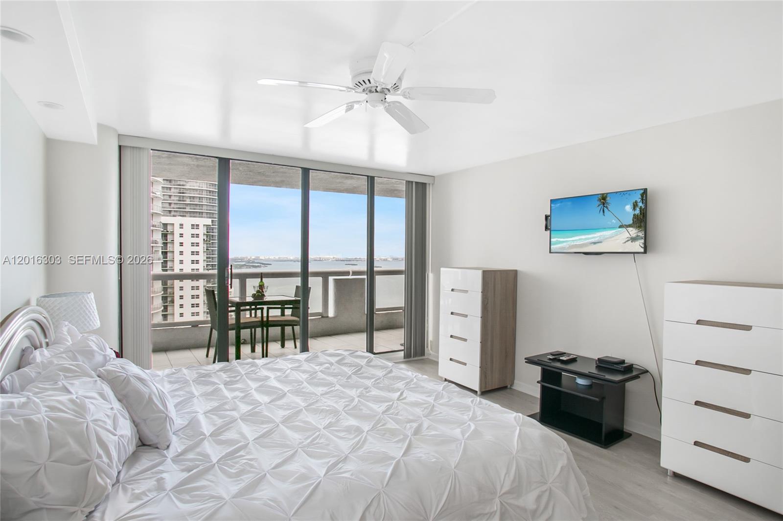 A bedroom features a bed, two dressers, a television, and a balcony overlooking the water — 1717 N Bayshore Dr # 3751, Miami FL 33132, MIAMI, FL