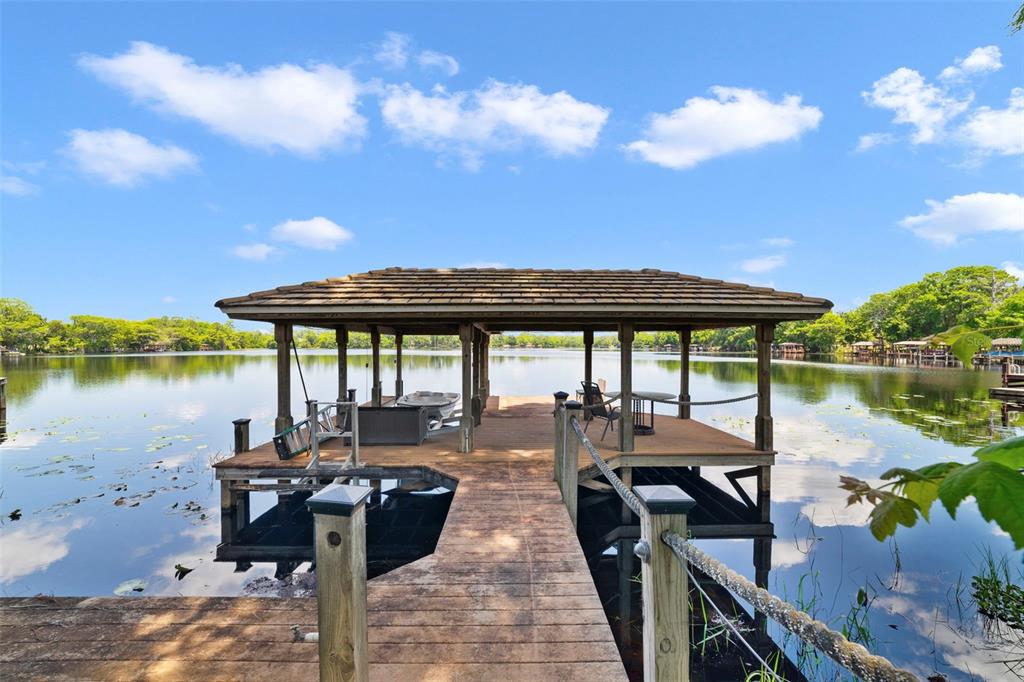 A wooden boat dock with a covered seating area extends over a calm lake — 3308 LUKAS COVE, ORLANDO, FL