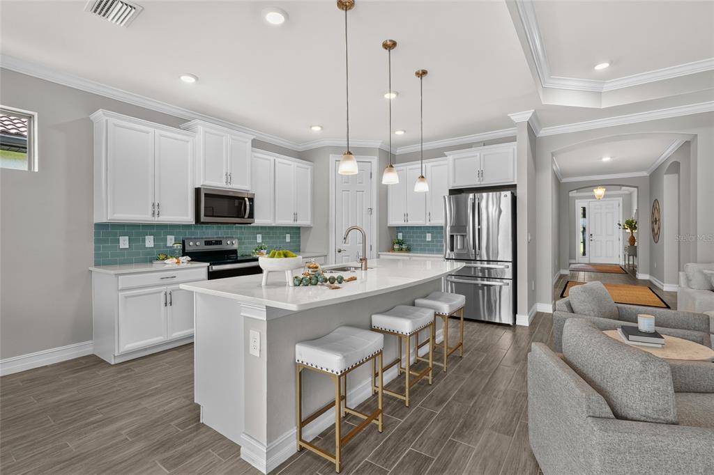 A modern kitchen features white cabinets, a central island with bar seating, and teal backsplash tile — 696 RAVELLO BOULEVARD, NOKOMIS, FL