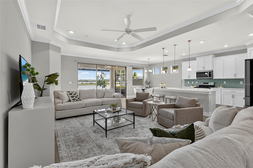 An open-concept living room and kitchen with a tray ceiling, neutral furniture, and water views — 696 RAVELLO BOULEVARD, NOKOMIS, FL