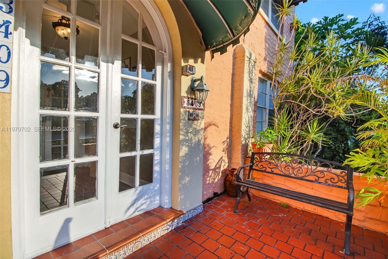 A white arched double door opens onto a red brick patio with a metal bench — 3409 S Le Jeune Rd, Coral Gables FL 33134, CORAL GABLES, FL