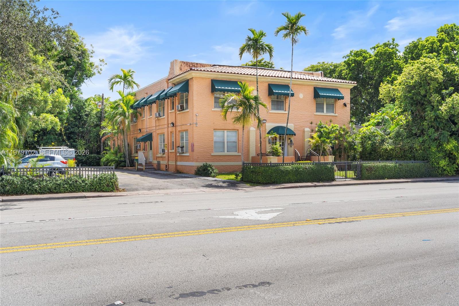 A two-story peach-colored apartment building with green awnings sits behind a low fence — 3409 S Le Jeune Rd, Coral Gables FL 33134, CORAL GABLES, FL