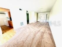 A living room with beige carpet, white walls, and an adjacent kitchen area — 24862 US HIGHWAY 19 N UNIT 3202, CLEARWATER, FL