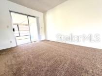 A carpeted room features a sliding glass door leading to an enclosed outdoor space — 24862 US HIGHWAY 19 N UNIT 3202, CLEARWATER, FL