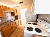 A kitchen features wood cabinets, a white electric stove, and a stainless steel sink — 24862 US HIGHWAY 19 N UNIT 3202, CLEARWATER, FL