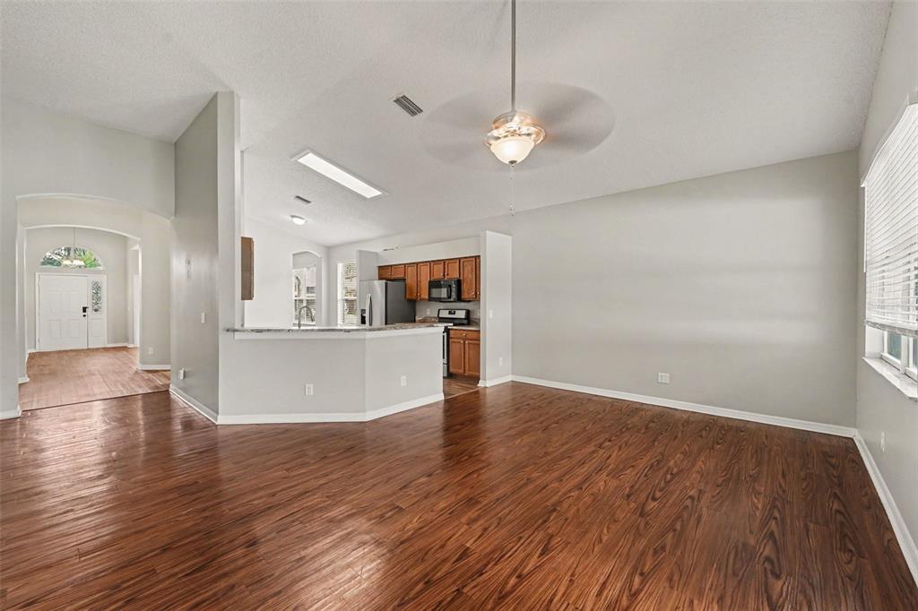 An open-concept living area features wood-look flooring, a ceiling fan, and a kitchen island — 4906 PENNECOTT WAY, WESLEY CHAPEL, FL