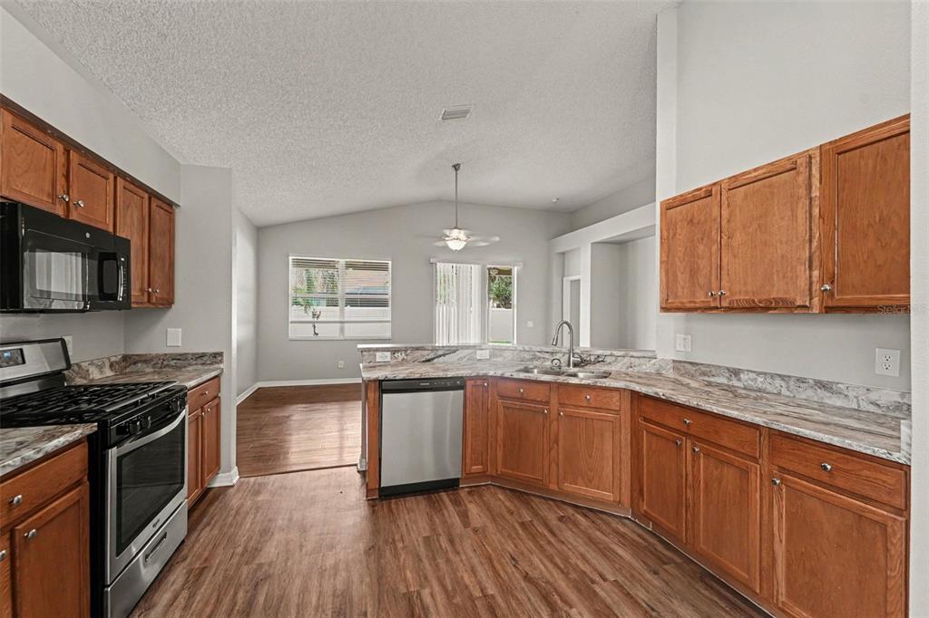 A kitchen with wood cabinets, laminate countertops, and stainless steel appliances opens to a living area — 4906 PENNECOTT WAY, WESLEY CHAPEL, FL