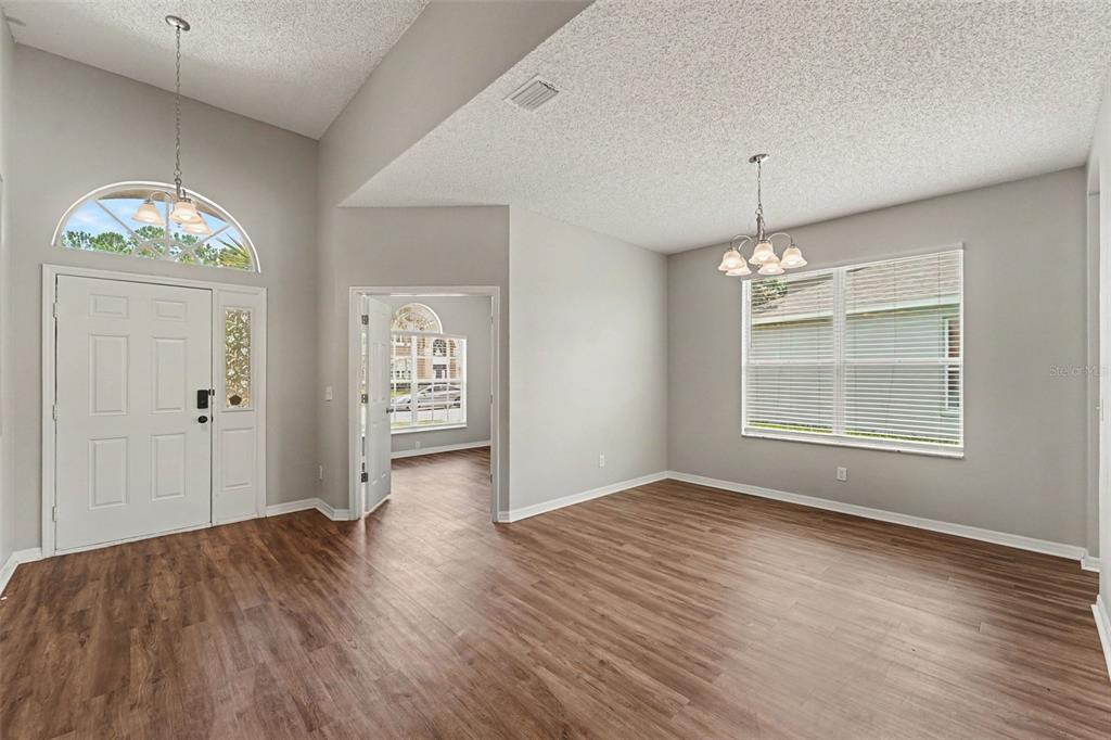 An entryway and dining area feature wood-look flooring, light gray walls, and vaulted ceilings — 4906 PENNECOTT WAY, WESLEY CHAPEL, FL