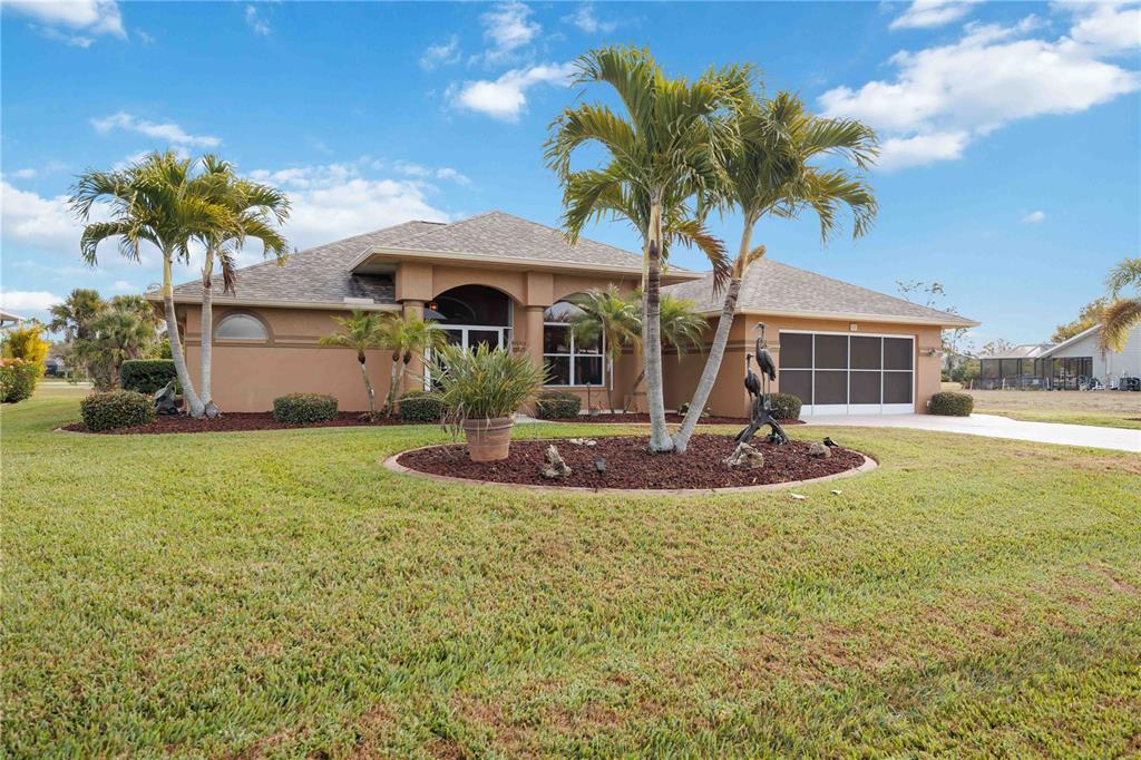 A single-story tan house features a screened garage door and palm trees in the yard — 55 CLUBHOUSE ROAD, ROTONDA WEST, FL