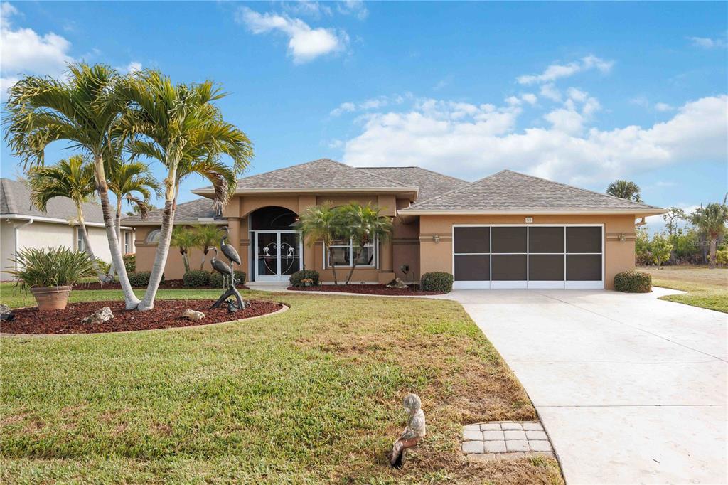 A single-story tan house with a multi-car garage, palm trees, and a landscaped front yard — 55 CLUBHOUSE ROAD, ROTONDA WEST, FL