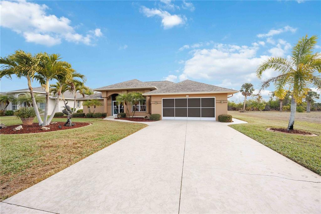 A single-story tan house with a screened garage door and palm trees in the yard — 55 CLUBHOUSE ROAD, ROTONDA WEST, FL