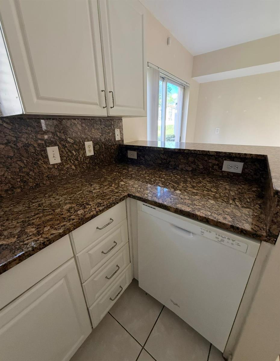 A kitchen features white cabinets, brown granite countertops, and a white dishwasher — 3481 Briar Bay Boulevard # 101, West Palm Beach FL 33411, WEST PALM BEACH, FL