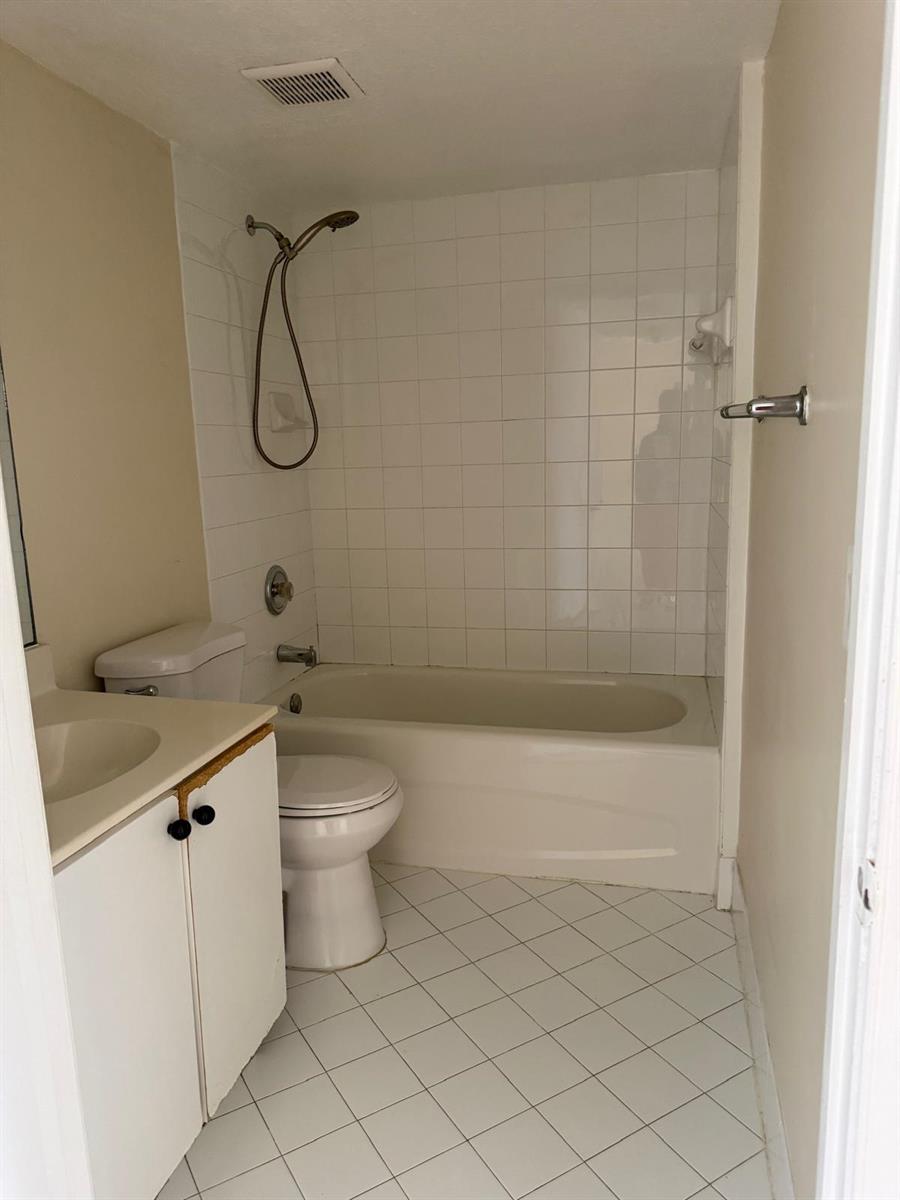 A bathroom features a white vanity, a toilet, and a bathtub with a shower head — 3481 Briar Bay Boulevard # 101, West Palm Beach FL 33411, WEST PALM BEACH, FL
