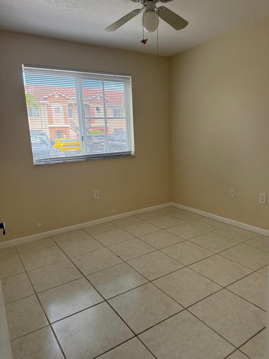An empty bedroom with beige walls, tile flooring, a ceiling fan, and a window — 3481 Briar Bay Boulevard # 101, West Palm Beach FL 33411, WEST PALM BEACH, FL