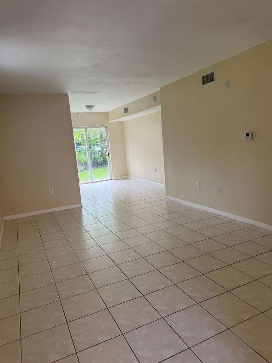 An empty living area features beige tile flooring, light-colored walls, and a sliding glass door — 3481 Briar Bay Boulevard # 101, West Palm Beach FL 33411, WEST PALM BEACH, FL