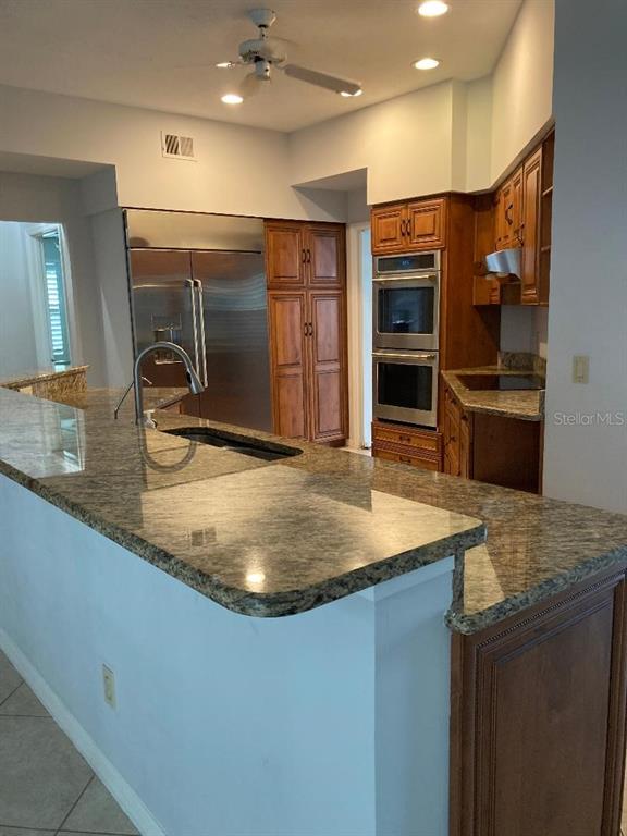 A kitchen features granite countertops, wood cabinetry, stainless steel appliances, and a ceiling fan — 224 HUNTRIDGE WAY, WINTER SPRINGS, FL