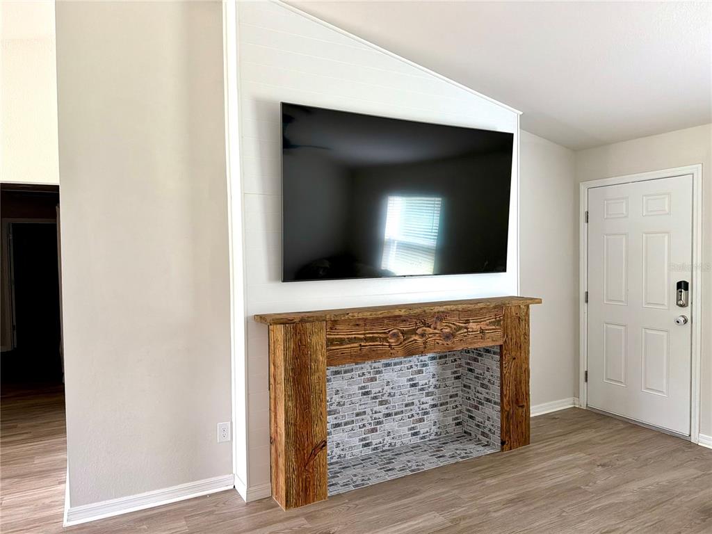A living room features a wall-mounted television above a rustic wooden fireplace mantel and hearth — 11034 CARNEGIE AVE., ENGLEWOOD, FL