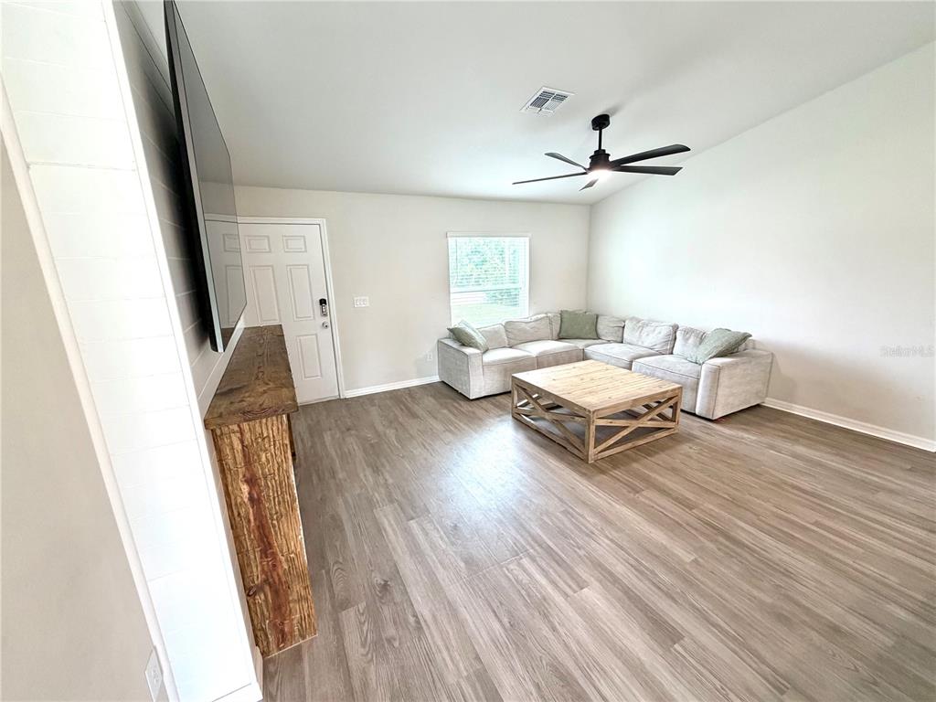 A living room features light wood-look flooring, a large sectional sofa, and a rustic wood mantel — 11034 CARNEGIE AVE., ENGLEWOOD, FL