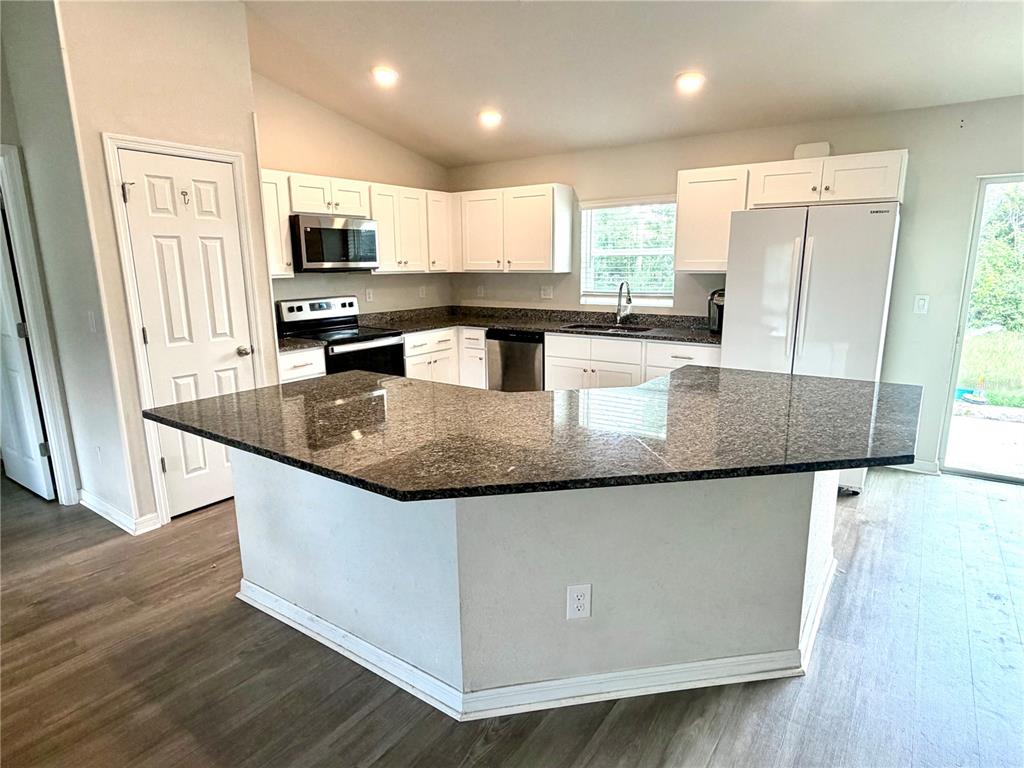 A kitchen features white cabinets, dark granite countertops, a breakfast bar, and stainless steel appliances — 11034 CARNEGIE AVE., ENGLEWOOD, FL