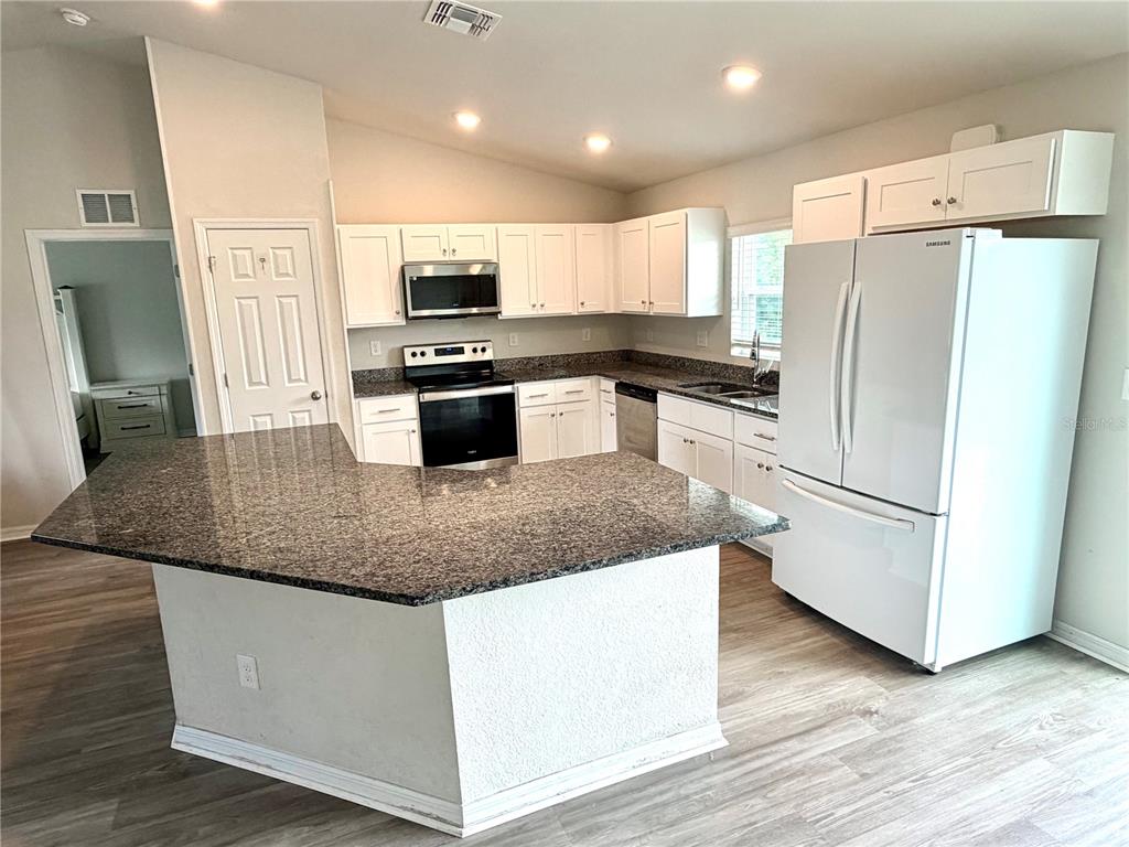 A kitchen features white cabinets, granite countertops, a kitchen island, and white appliances — 11034 CARNEGIE AVE., ENGLEWOOD, FL