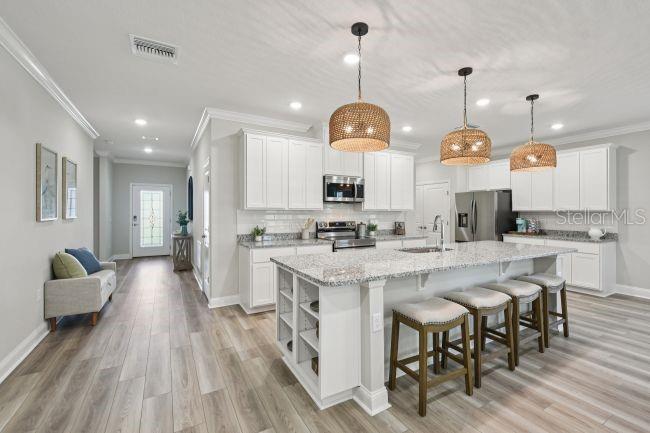 A modern kitchen features white cabinets, granite countertops, a large island, and three woven pendant lights — 8592 OAKSTONE CIRCLE, LEESBURG, FL