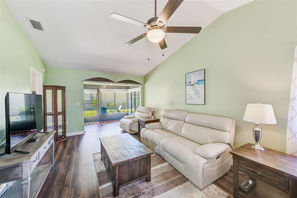 A living room features light green walls, wood-look flooring, a white sofa, and a ceiling fan — 6040 27TH STREET W, BRADENTON, FL