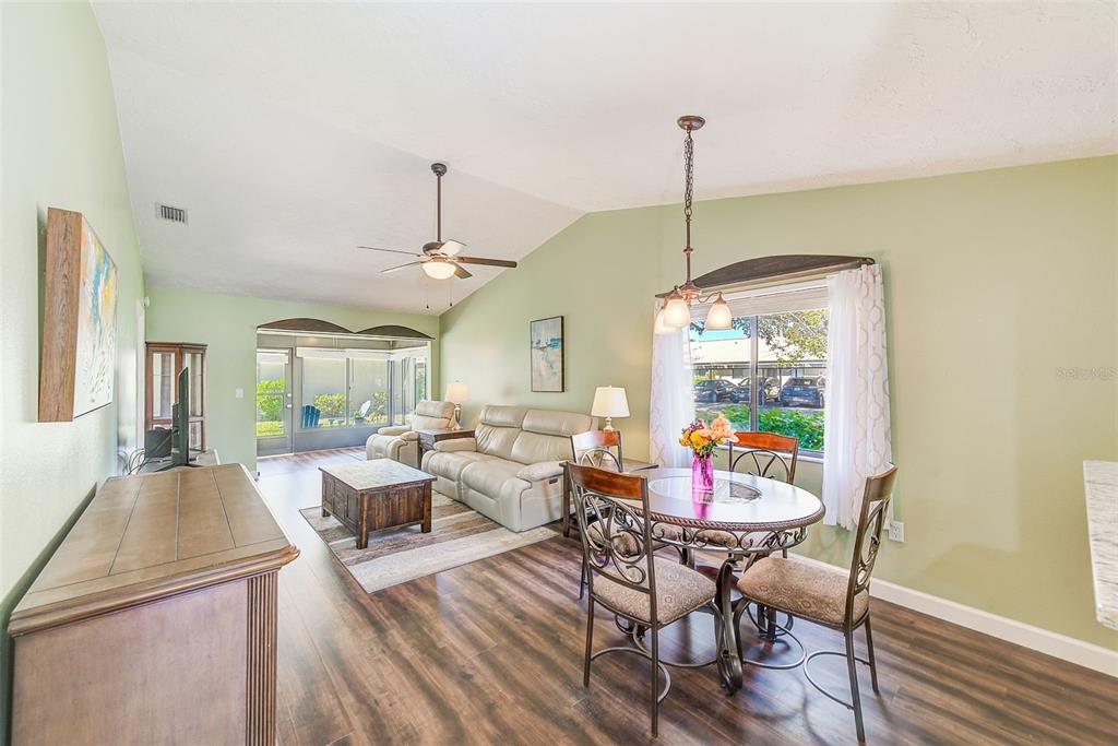A living and dining area with light green walls, wood-look flooring, and a vaulted ceiling — 6040 27TH STREET W, BRADENTON, FL