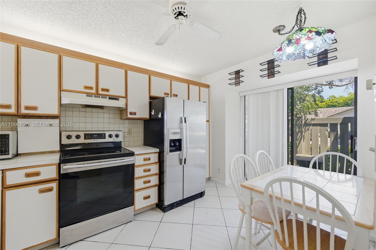 A kitchen features white cabinets with wood trim, stainless steel appliances, and a dining area — 4790 NW 22nd St, Coconut Creek FL 33063, COCONUT CREEK, FL
