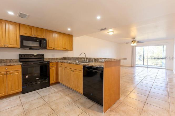 A kitchen with light wood cabinets, black appliances, and tile flooring opens to a living area — 6800 PLACIDA ROAD UNIT 168, ENGLEWOOD, FL