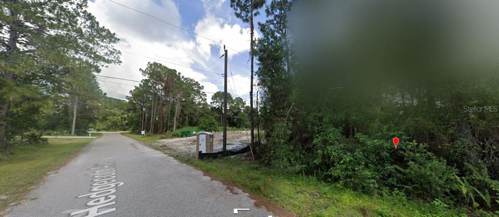 A gravel road leads past a portable toilet and a wooded lot with a red marker — HEDGECOTH AVENUE, NORTH PORT, FL