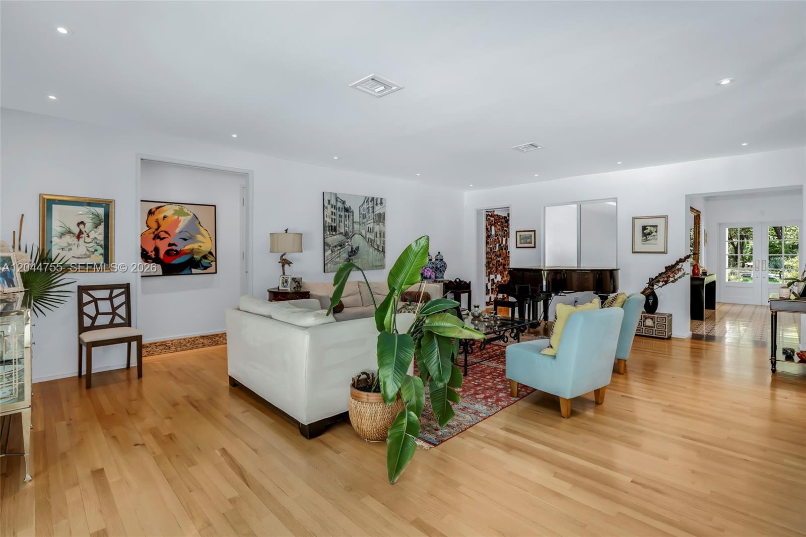A bright living room features hardwood floors, a white sofa, blue armchairs, and a piano — 12121 SW 64th Ave, Pinecrest FL 33156, PINECREST, FL