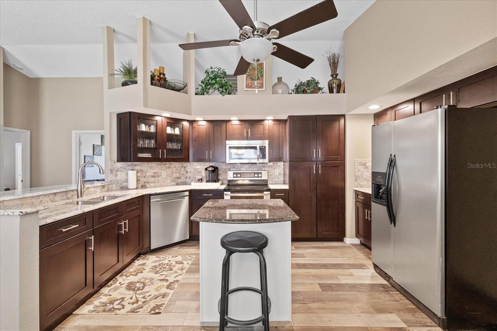 A kitchen features dark wood cabinets, stainless steel appliances, a center island, and high ceilings — 3251 SCORECARD DRIVE, NEW PORT RICHEY, FL