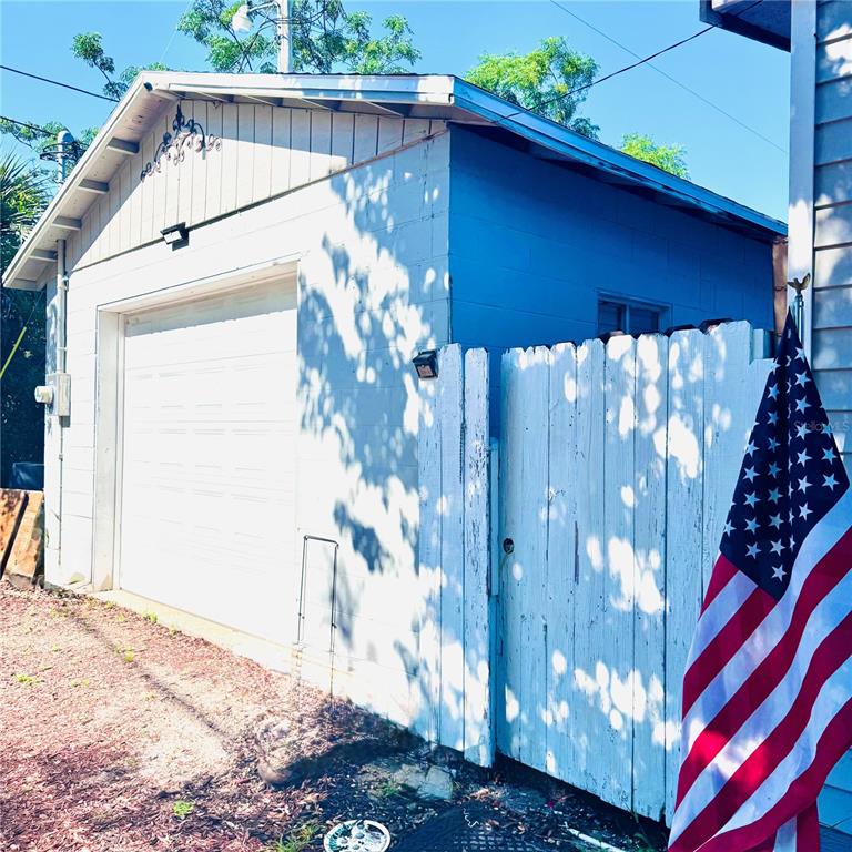 A detached garage with a white door and blue siding stands next to a wooden fence — 1301 AVENUE D, ORMOND BEACH, FL