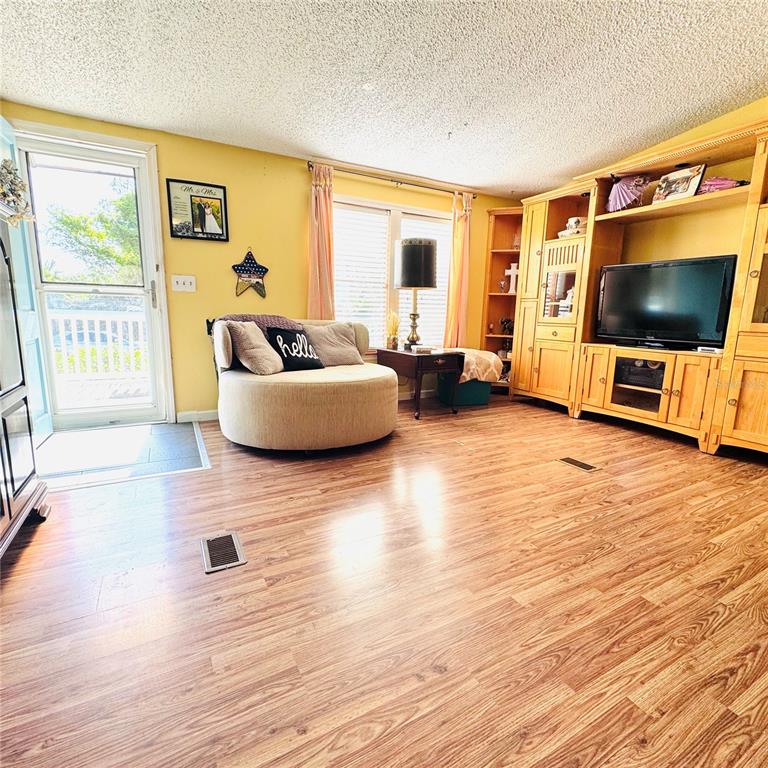 A living room features wood-look flooring, yellow walls, a round chair, and a large entertainment center — 1301 AVENUE D, ORMOND BEACH, FL