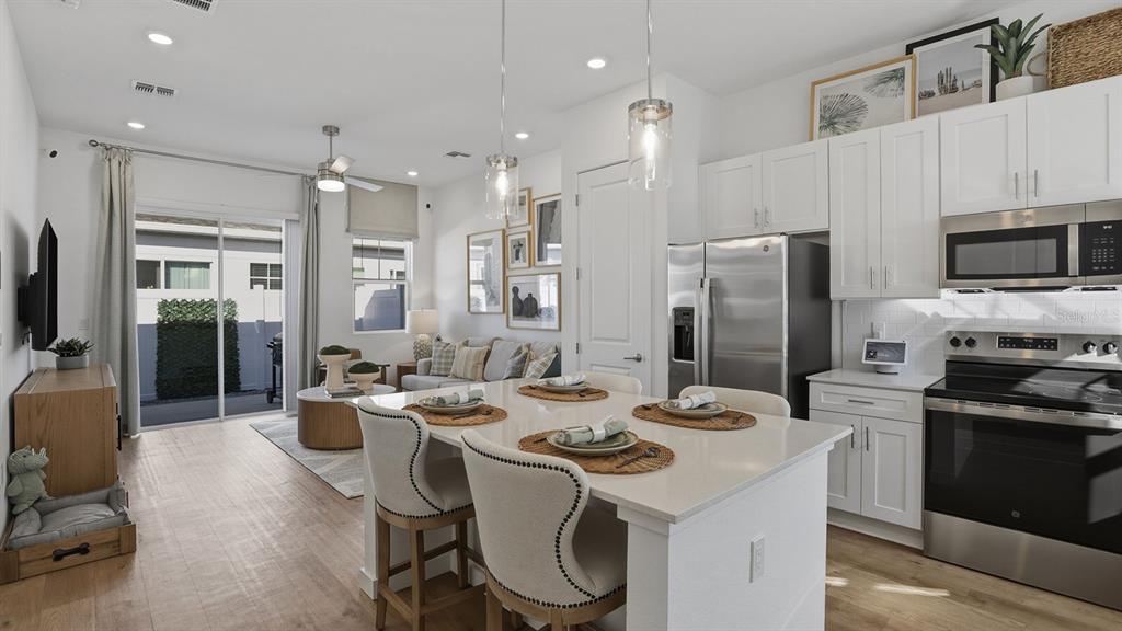 A bright open-concept kitchen and living area features white cabinetry, stainless appliances, and wood flooring — 2507 KOJI STREET UNIT Aspire, MOUNT DORA, FL