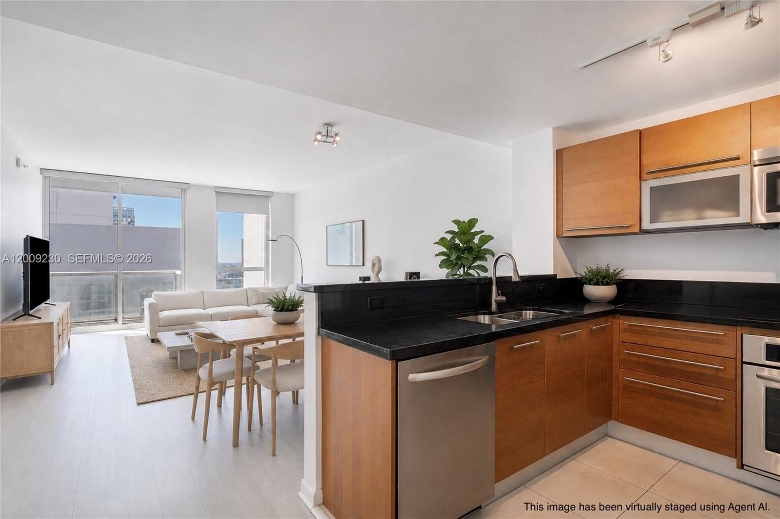 A kitchen with wood cabinets and black countertops overlooks a living and dining area — 253 NE 2nd St # 3104, Miami FL 33132, MIAMI, FL