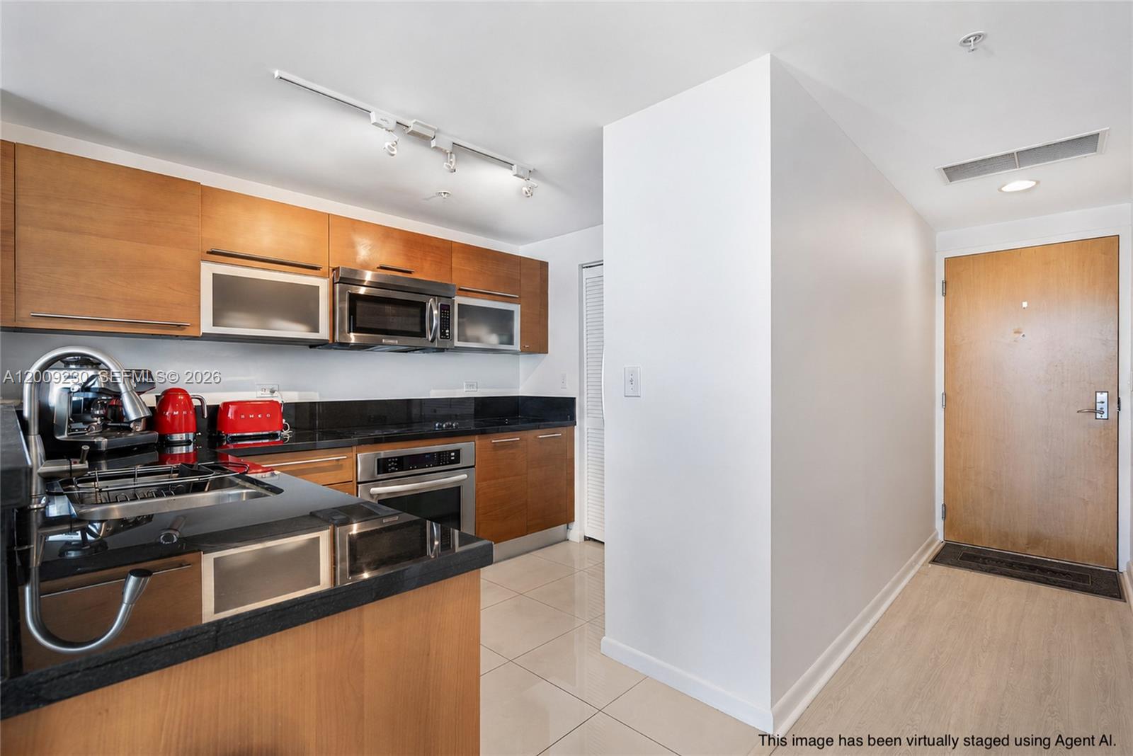 A kitchen with wood cabinets, black countertops, and stainless steel appliances next to an entryway — 253 NE 2nd St # 3104, Miami FL 33132, MIAMI, FL