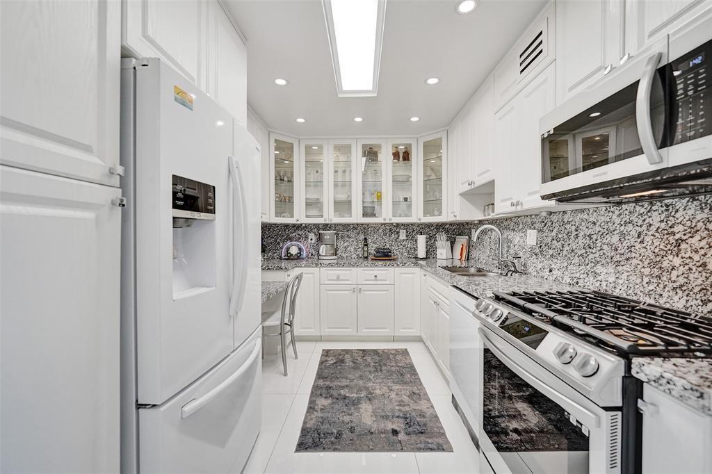 A white kitchen features granite countertops, stainless steel appliances, and glass-front upper cabinets — 2030 S Ocean Drive # 510, Hallandale Beach FL 33009, HALLANDALE BEACH, FL