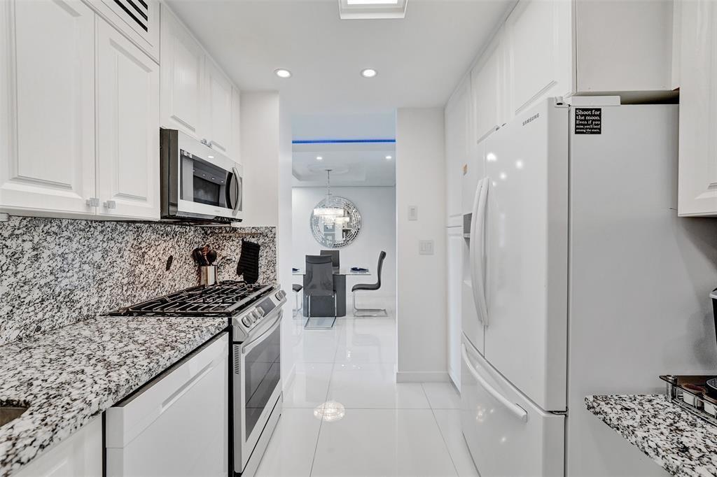 A white galley kitchen features granite countertops, stainless steel appliances, and a view into a dining area — 2030 S Ocean Drive # 510, Hallandale Beach FL 33009, HALLANDALE BEACH, FL