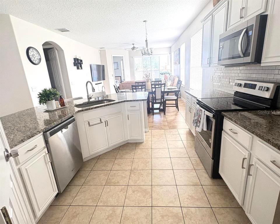 A kitchen with white cabinets, granite countertops, and stainless steel appliances overlooks a dining area — 2248 STONE LAKE COURT, ORLANDO, FL