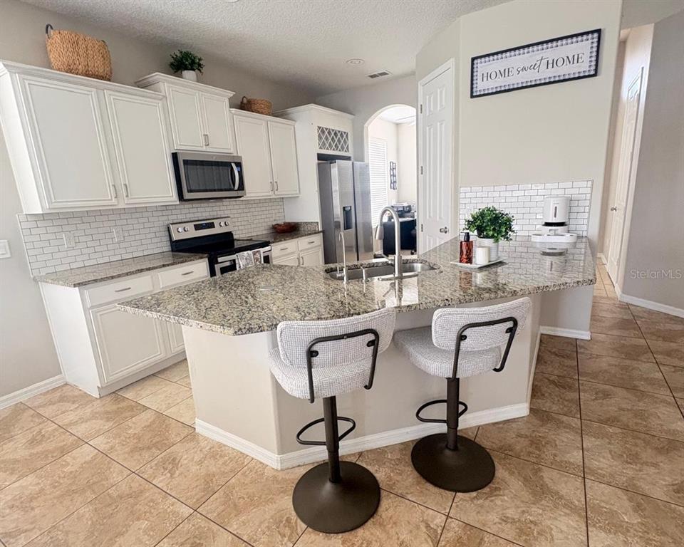 A kitchen features white cabinets, granite countertops, a central island with bar stools, and tile flooring — 2248 STONE LAKE COURT, ORLANDO, FL