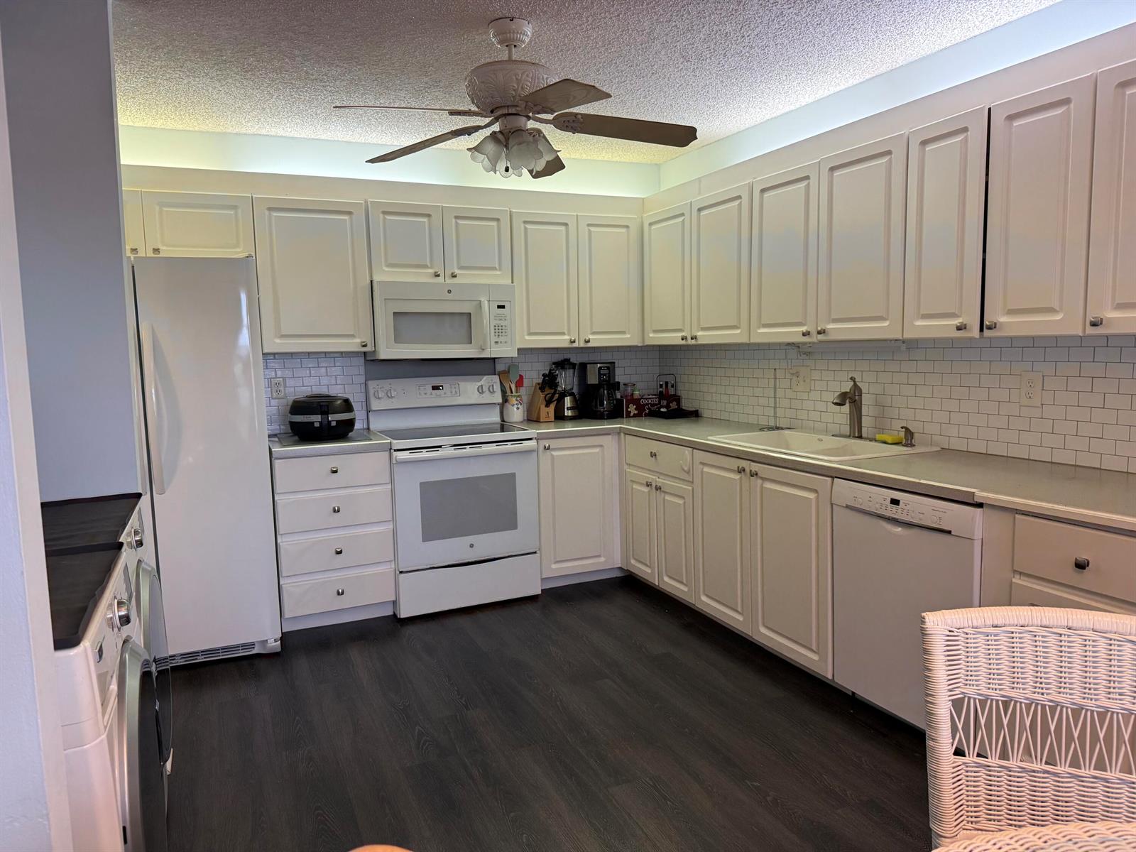A kitchen features white cabinetry, a subway tile backsplash, dark flooring, and white appliances — 1520 NW 19th Terrace # 203, Delray Beach FL 33445, DELRAY BEACH, FL