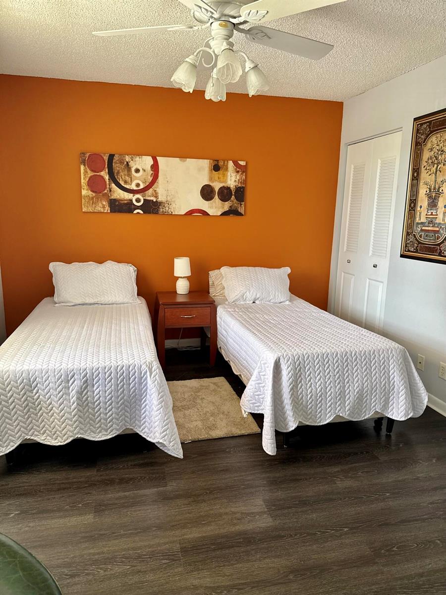 A bedroom features two twin beds, a central nightstand, and an orange accent wall — 1520 NW 19th Terrace # 203, Delray Beach FL 33445, DELRAY BEACH, FL