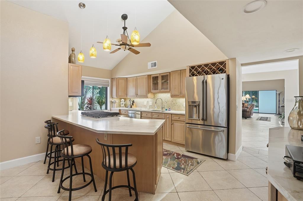 A kitchen with light wood cabinets, stainless steel appliances, a breakfast bar, and vaulted ceilings — 25188 MARION AVENUE UNIT 10, PUNTA GORDA, FL