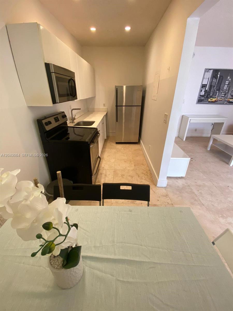 A small kitchen features white cabinets, stainless steel appliances, and a black stove — 934 Michigan Ave # 308, Miami Beach FL 33139, MIAMI BEACH, FL
