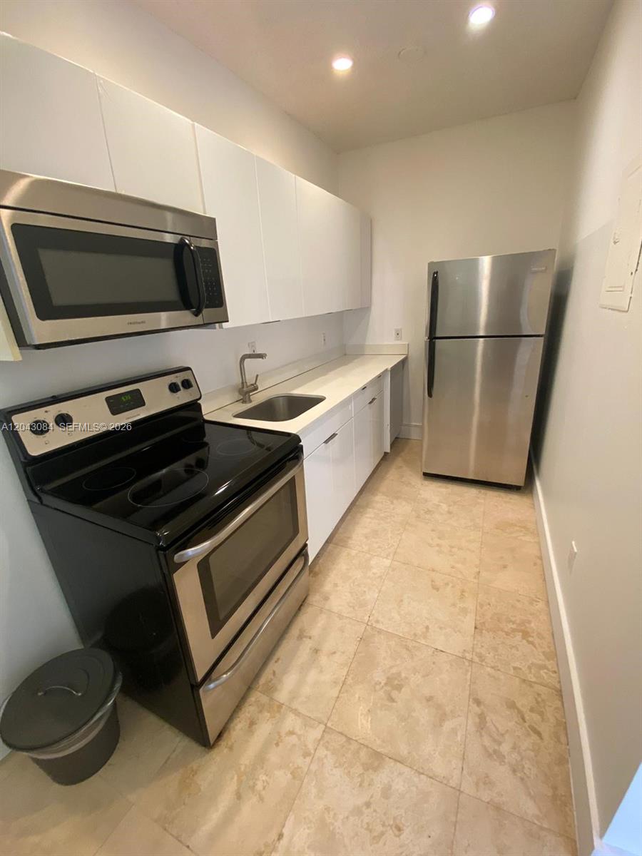 A galley-style kitchen features white cabinets, stainless steel appliances, and light-colored tile flooring — 934 Michigan Ave # 308, Miami Beach FL 33139, MIAMI BEACH, FL