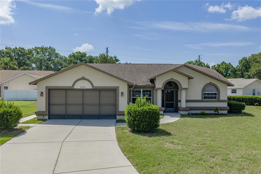 A single-story house with a two-car garage, beige stucco exterior, and a front entryway — 6232 HUNTINGTON DRIVE, ZEPHYRHILLS, FL