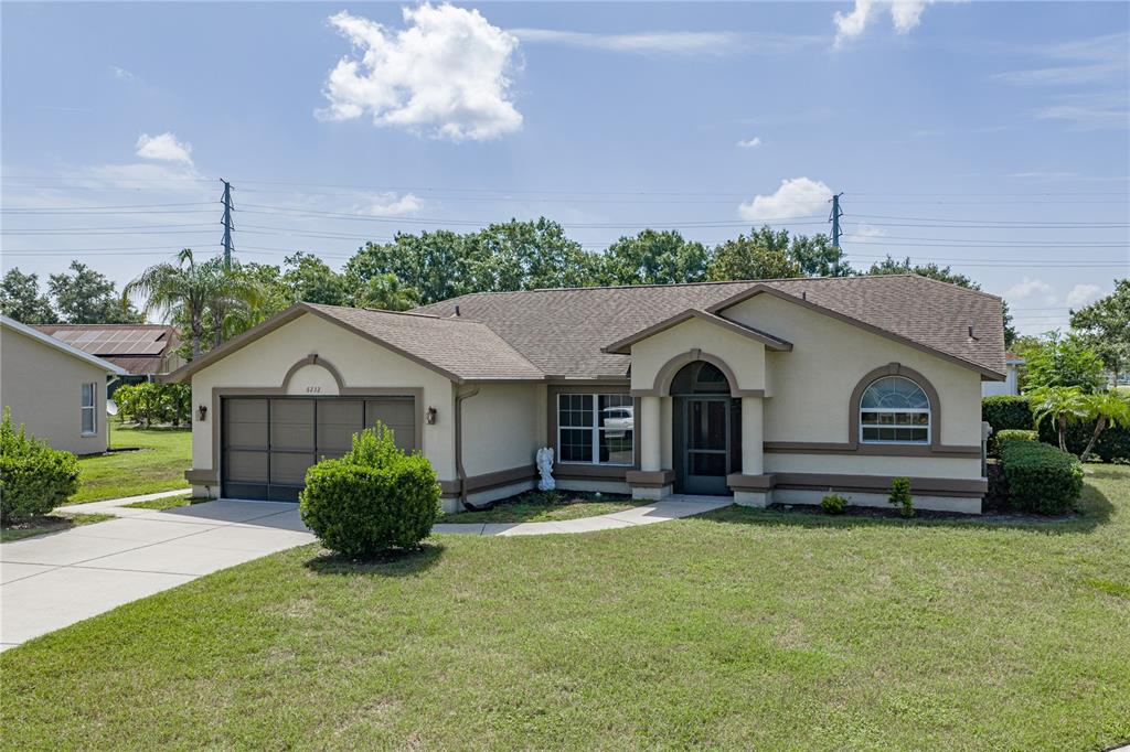 A single-story house with a tan stucco exterior, a brown roof, and a two-car garage — 6232 HUNTINGTON DRIVE, ZEPHYRHILLS, FL