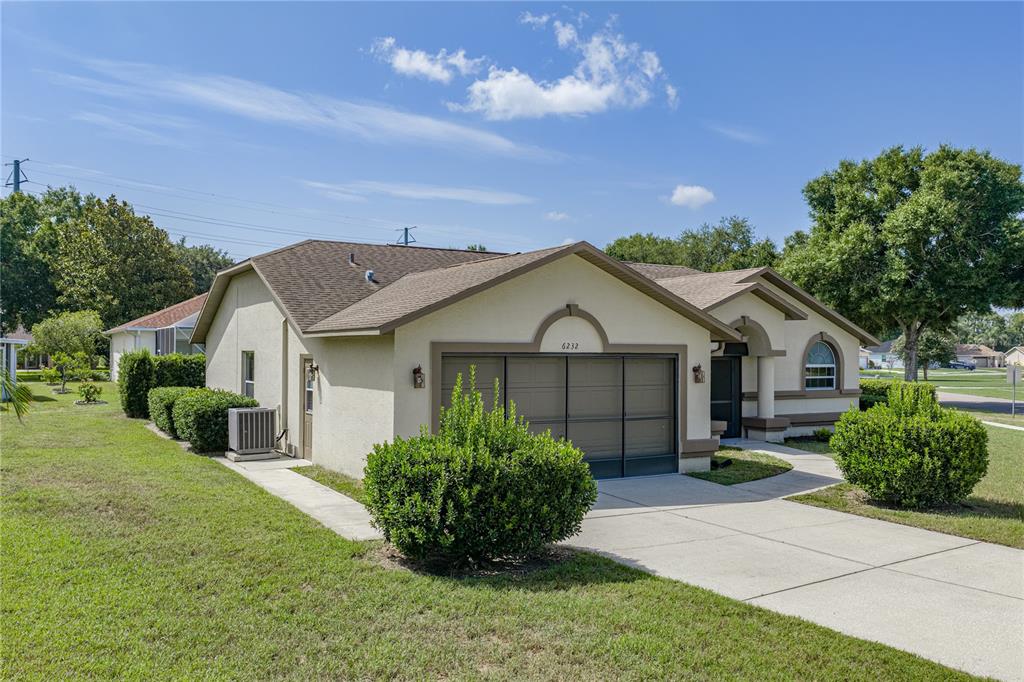 A single-story house with a tan stucco exterior, a brown roof, and a front garage — 6232 HUNTINGTON DRIVE, ZEPHYRHILLS, FL