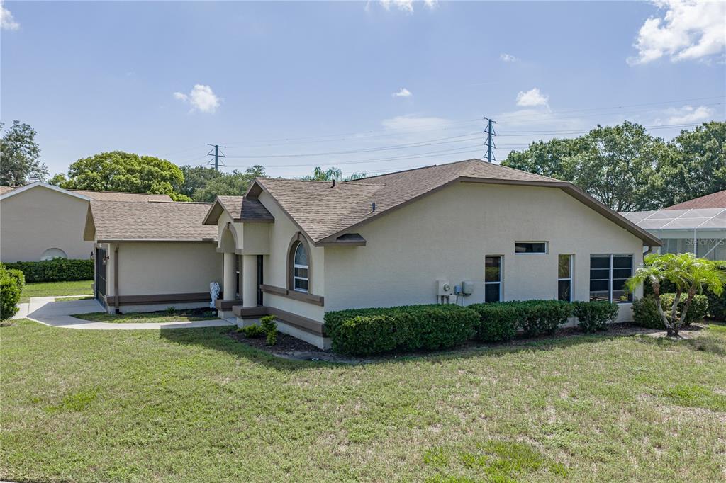 A side view of a tan stucco house with a brown shingled roof and landscaping — 6232 HUNTINGTON DRIVE, ZEPHYRHILLS, FL